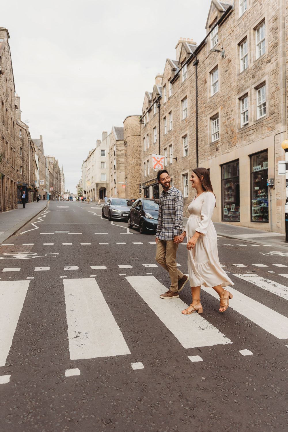 A couple walks across a zebra crossing on a historic Edinburgh street lined with stone buildings.