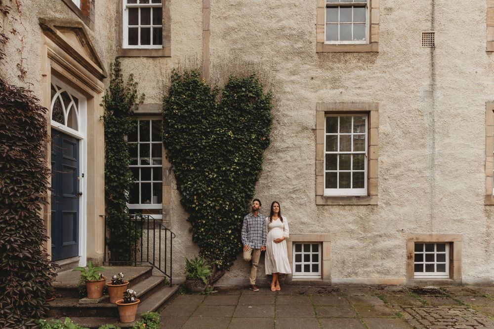 A couple stands together outside a historic ivy-covered stone building with Georgian windows and a blue door.