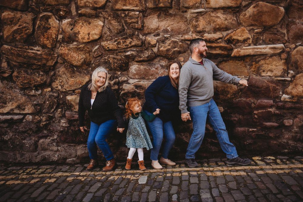 A group stands against a rustic stone wall on a cobblestone street.