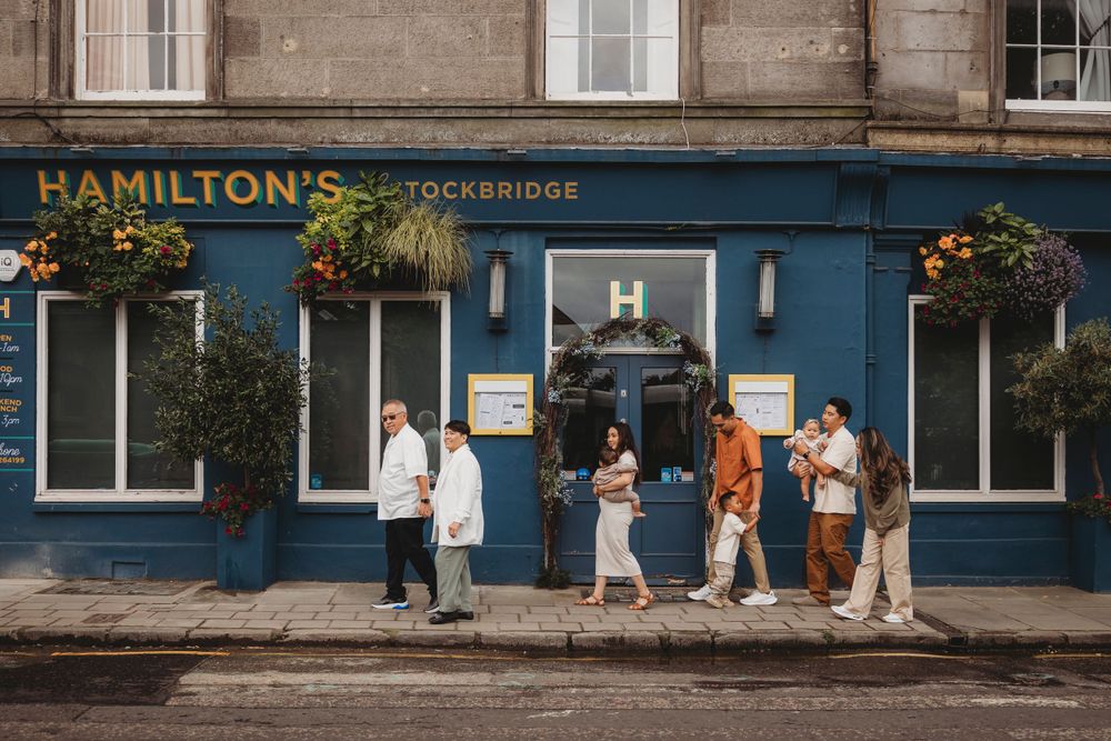 People gather outside Hamilton's, a charming blue-fronted storefront with hanging flower baskets.