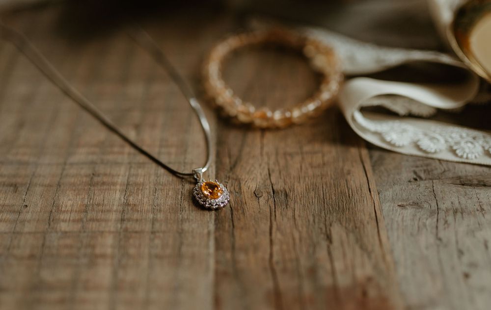 Close-up of a delicate silver pendant necklace with an amber gemstone on a rustic wooden surface.