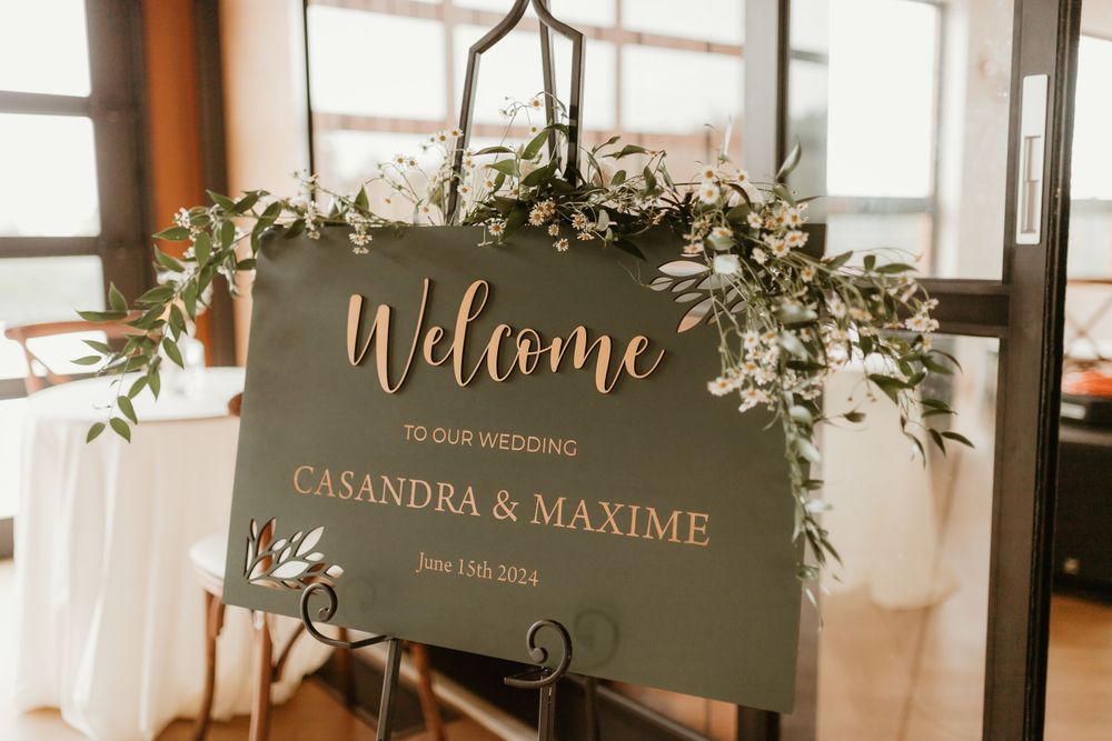 Elegant wedding welcome sign for Casandra and Maxime decorated with greenery and white flowers.
