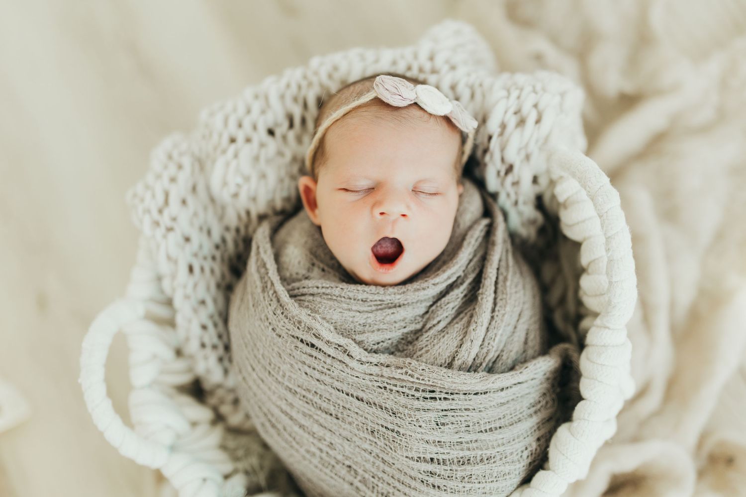 A sleeping newborn swaddled in a soft pink blanket rests peacefully in a rustic wooden drawer.