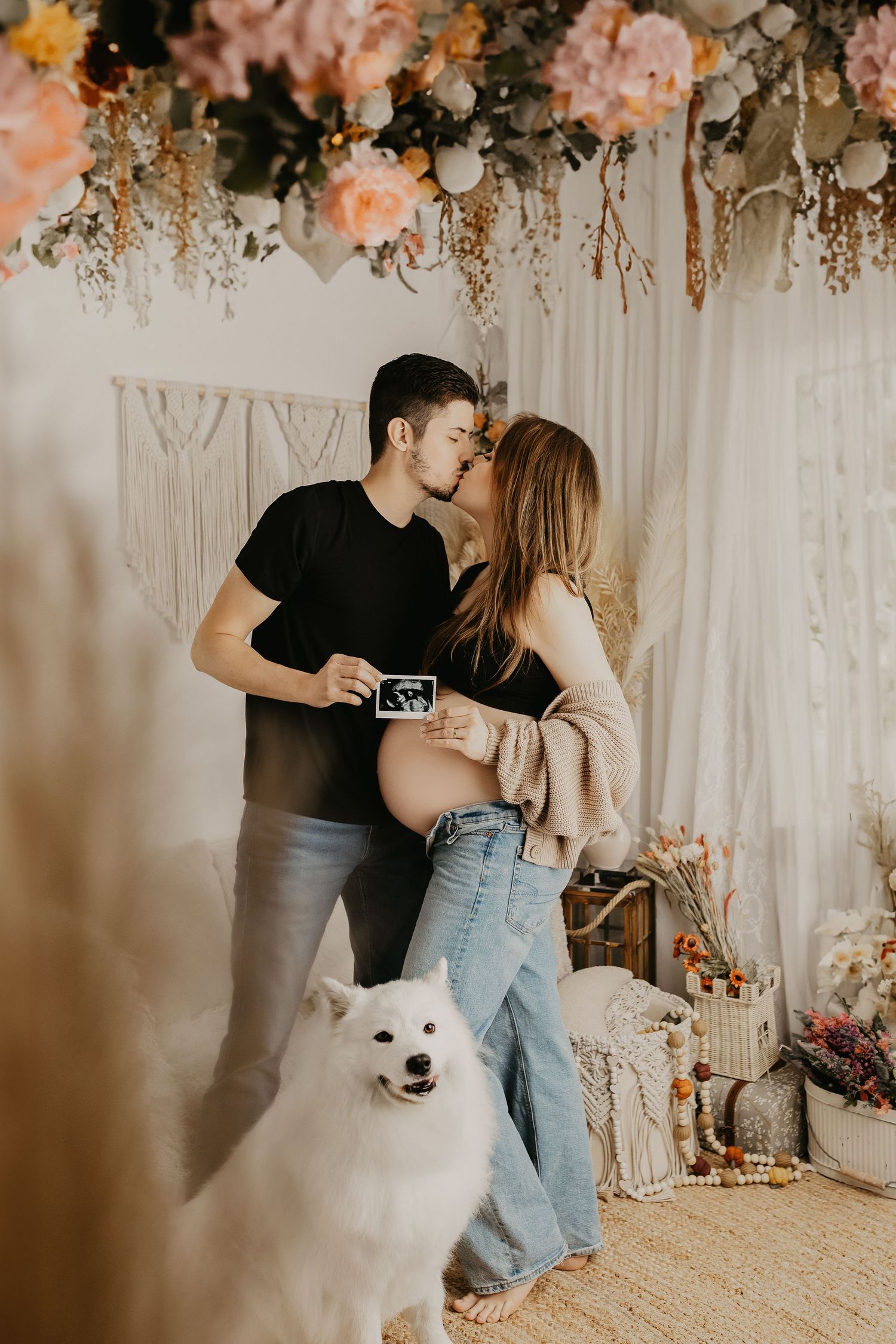 Romantic maternity photo with couple holding ultrasound while white dog sits nearby.