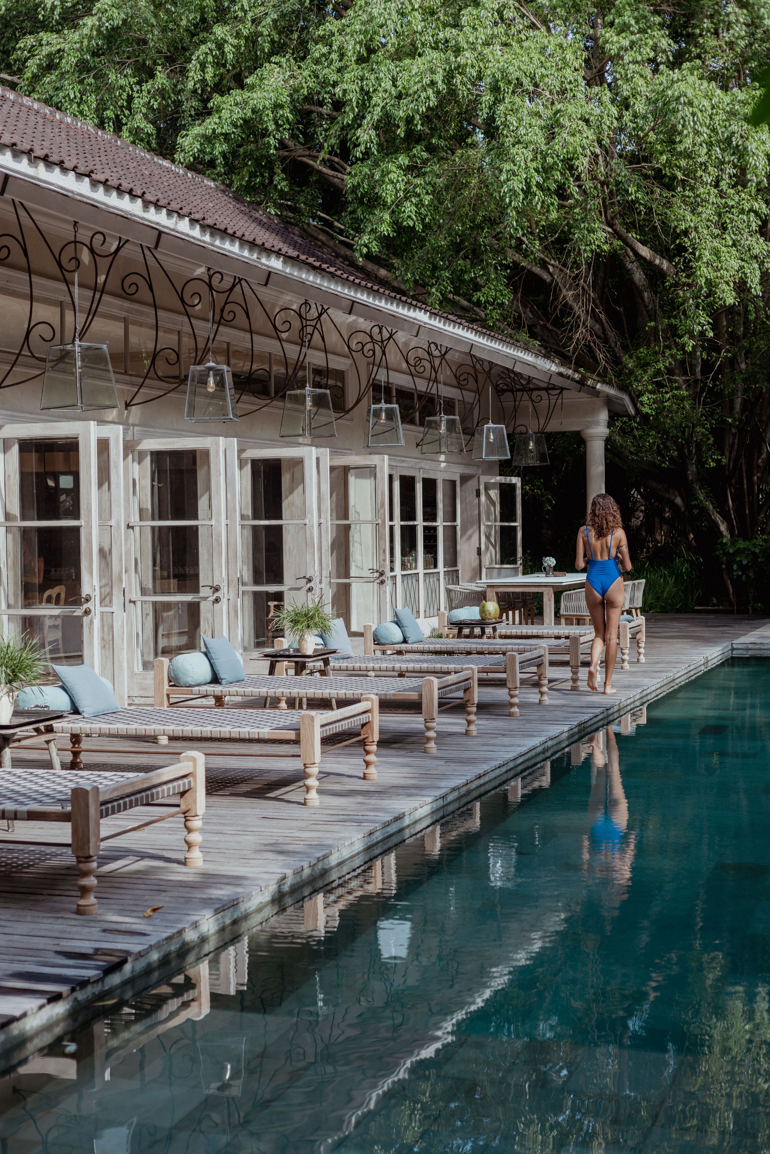 Luxurious poolside terrace with wooden loungers and white colonial architecture surrounded by lush greenery.