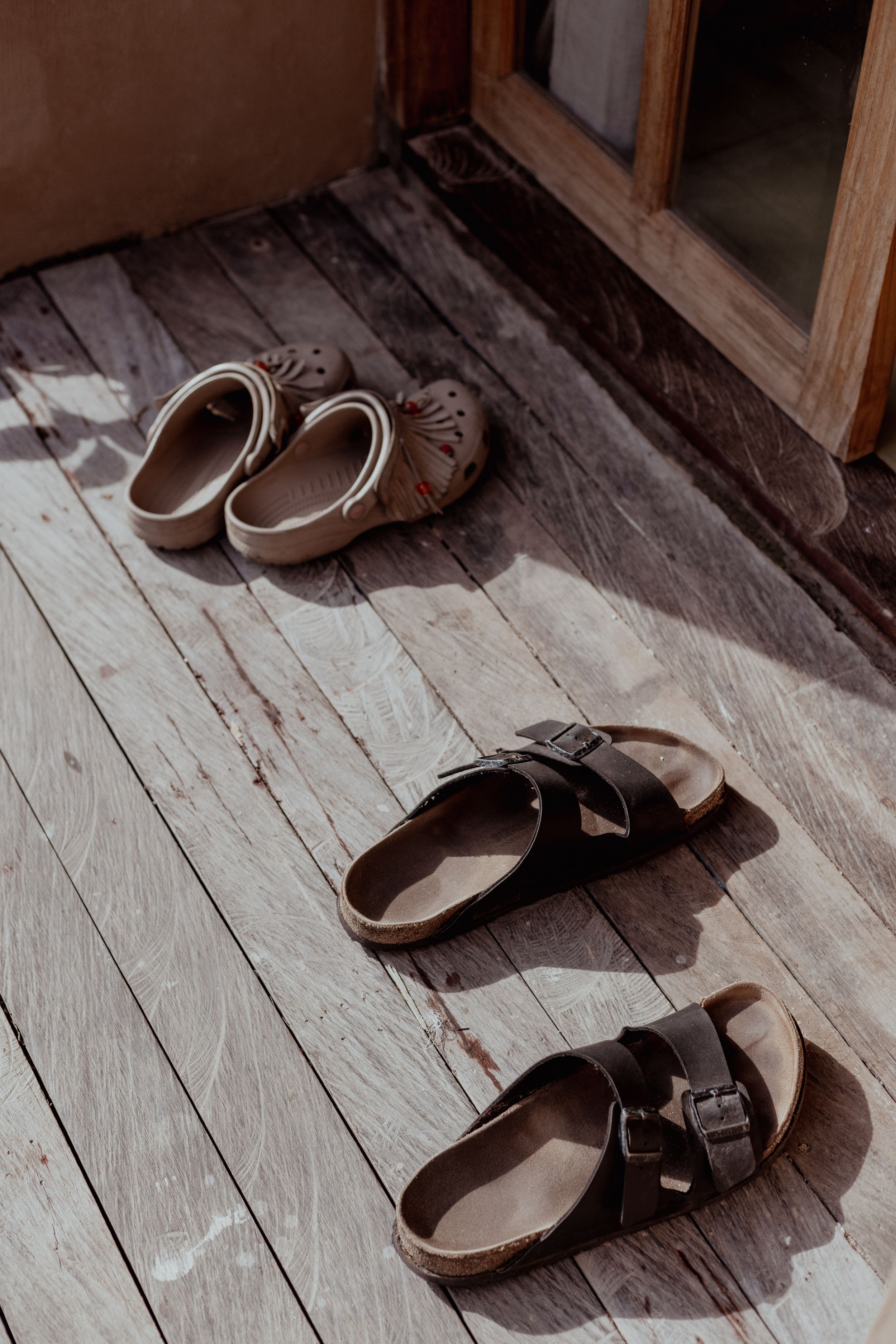 Pair of brown sandals and slippers arranged on a weathered wooden floor.