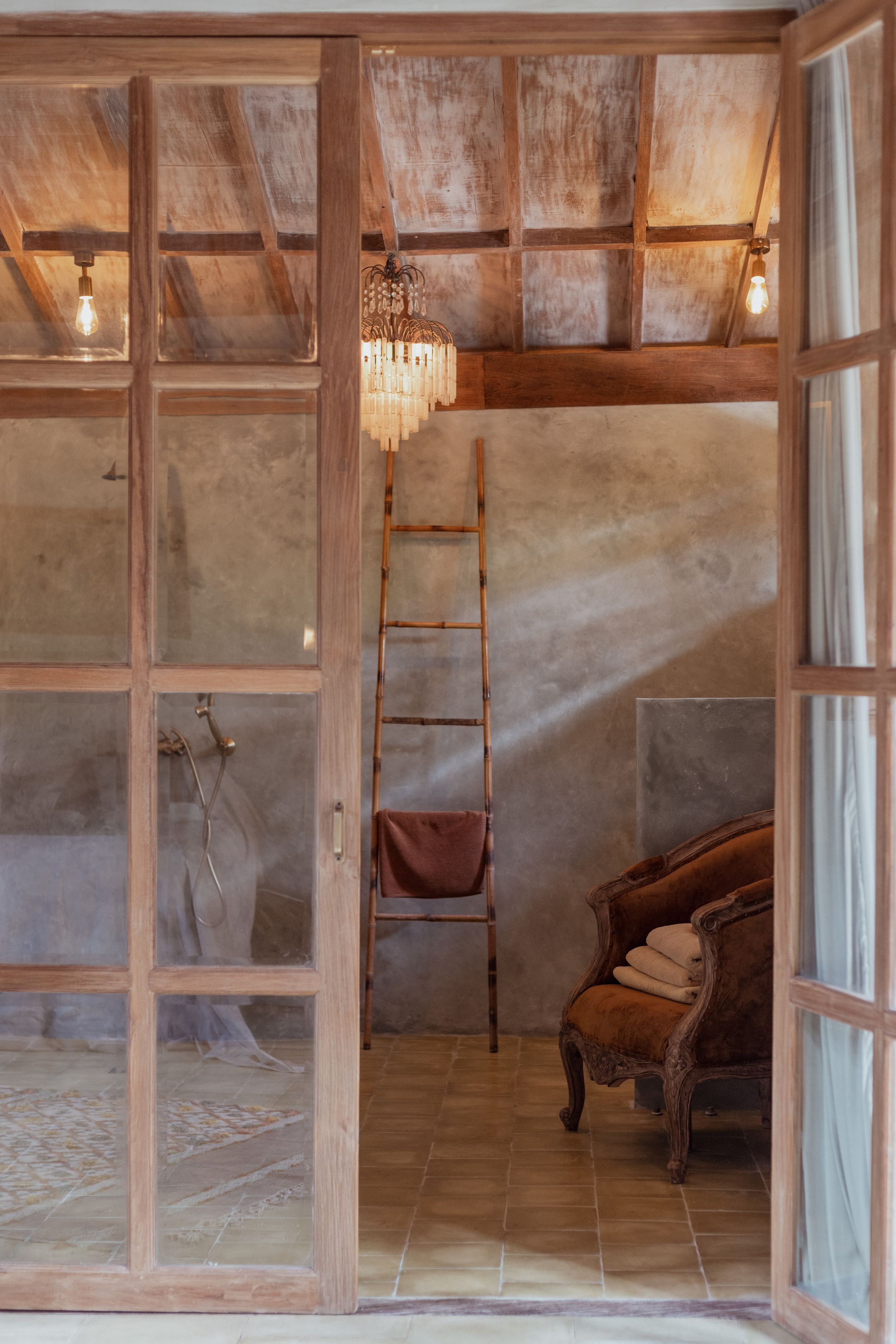 Rustic interior with wooden panels, crystal chandelier, vintage furniture and ladder against textured walls.