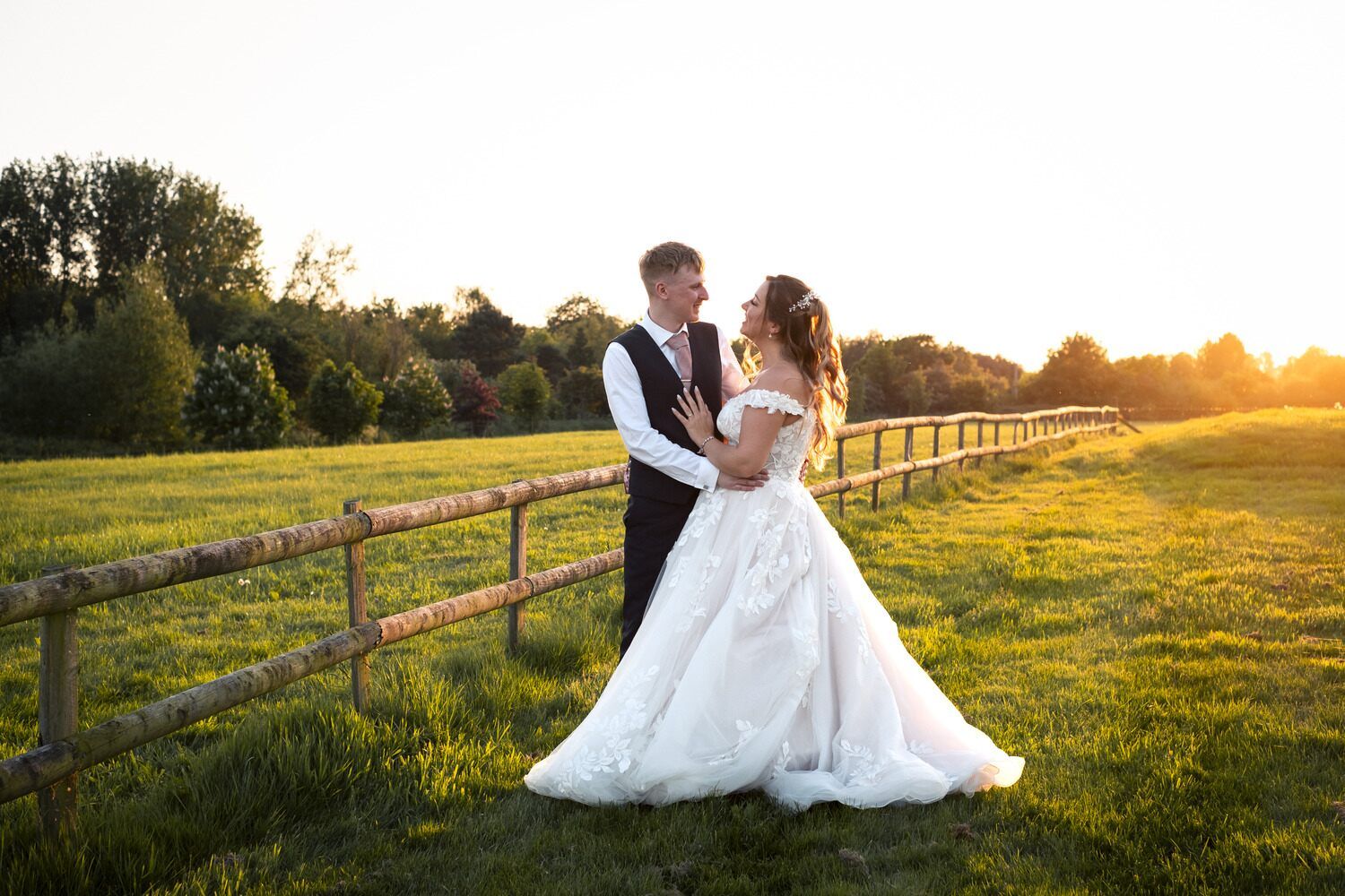 The newlyweds embrace in a field as the sun sets, casting a romantic golden glow over the scene.
