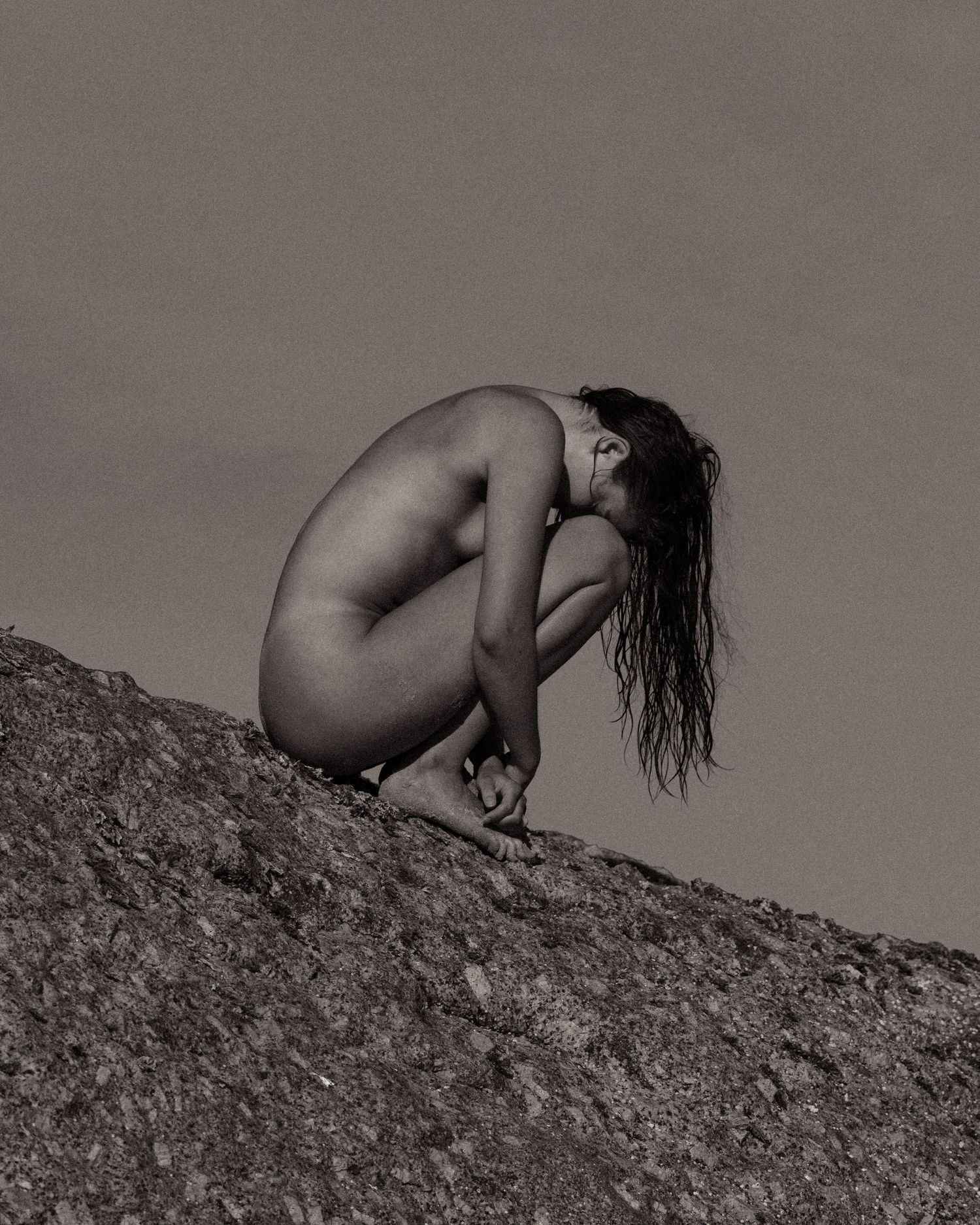 Artistic black and white photograph of a silhouetted figure crouching on a rocky surface.