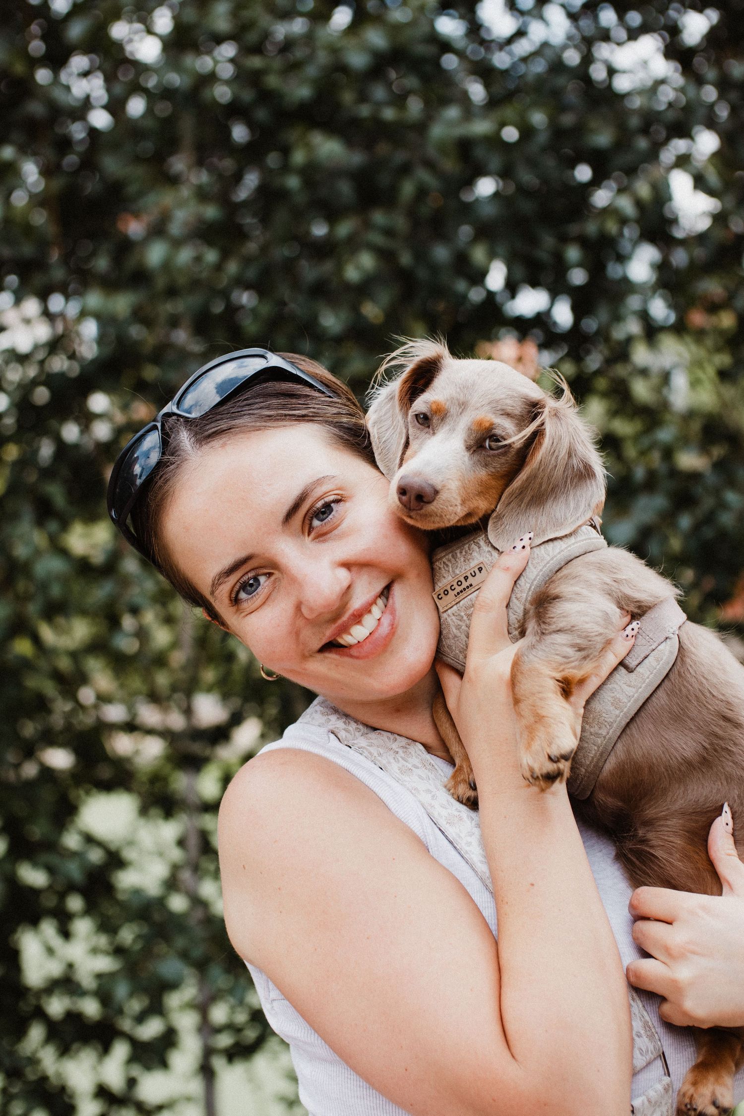 Woman in a pale top cuddling and sharing affectionate moments with a small brown dachshund dog in outdoor garden setting.