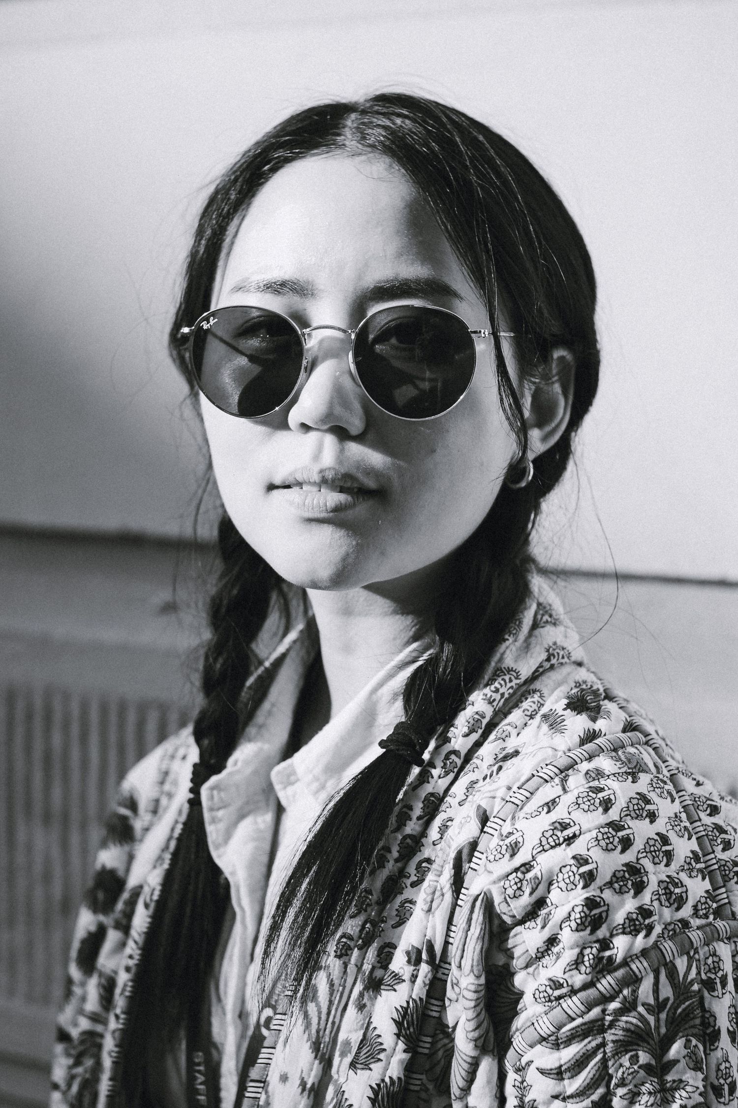 Black and white portrait showing a female in sunglasses and patterned jacket.