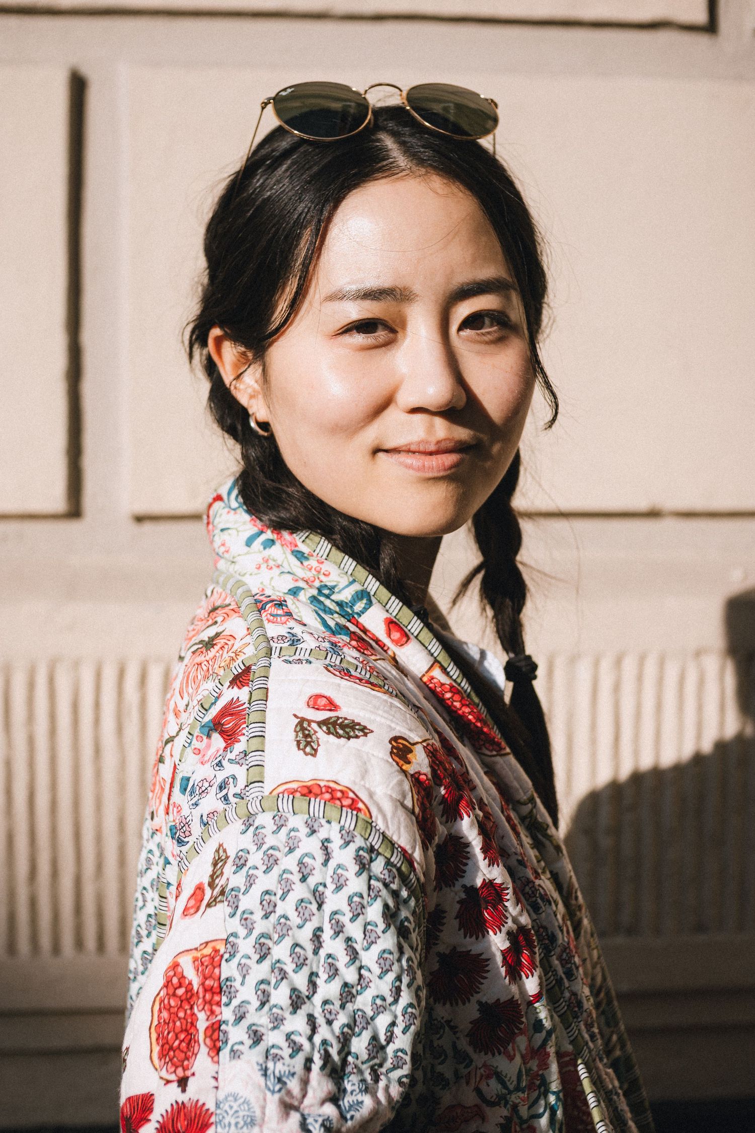 Portrait of a woman in a colourful floral and paisley patterned jacket with long dark platted hair.