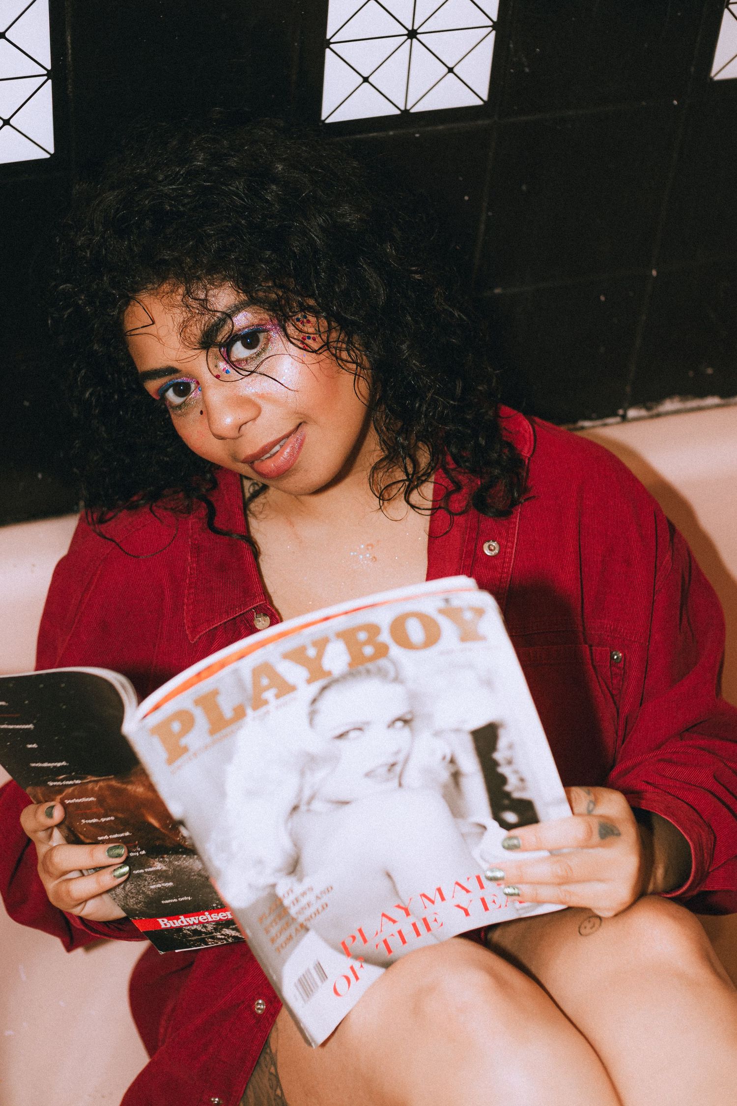 Portrait showing a woman wearing a red shirt in a bathtub reading a vintage Playboy magazine.