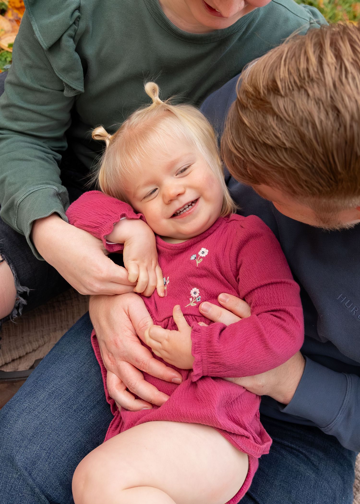 A child in a pink sweater laughs while being held on her parents lap