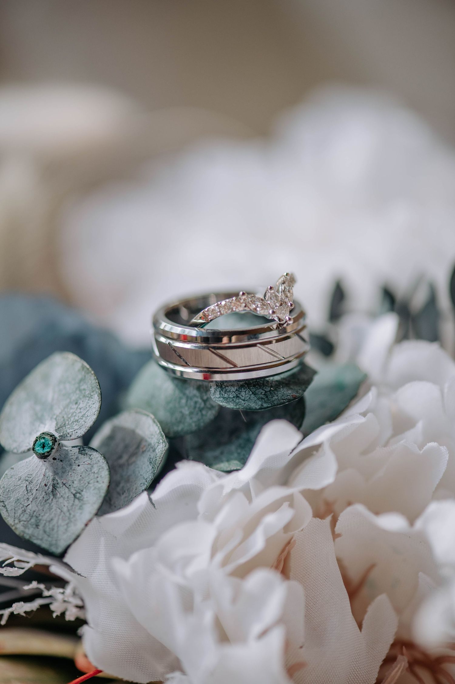 Elegant wedding rings nestled among white flowers and eucalyptus leaves.