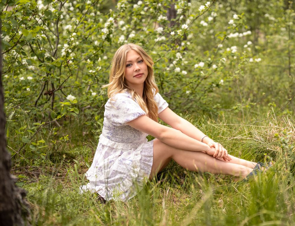 A person in a white dress sitting in a blooming spring meadow.