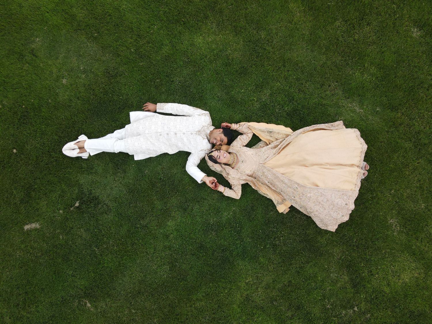 Aerial view of couple in wedding attire laying on green lawn.
