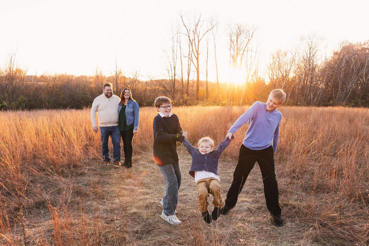 Family having fun at sunset in a golden field as they swing their child between them. Twin Cities, Decorah Iowa family photographer
