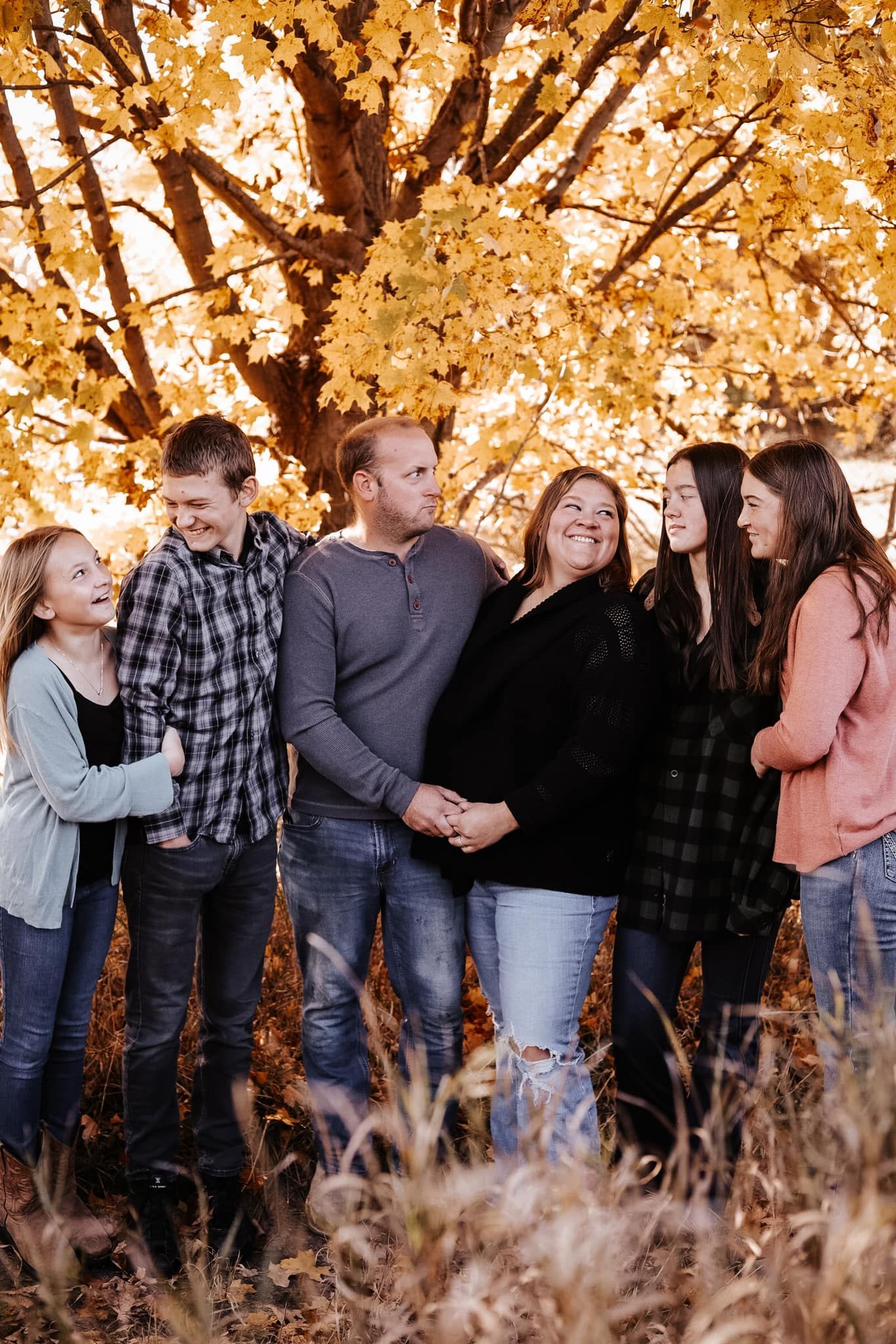 Family of six posing together under tree with golden autumn foliage.
