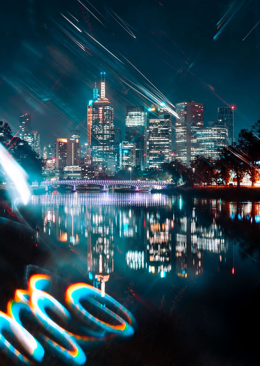 Illuminated city skyline at night reflected in calm river water, with light streaks, a lit bridge and glowing blue and orange neon swirls.