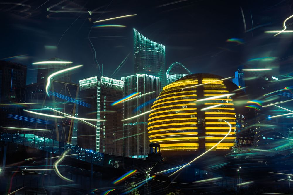 Long exposure night photo of a glowing golden spherical building and illuminated skyscrapers with colorful light trails in a modern city.