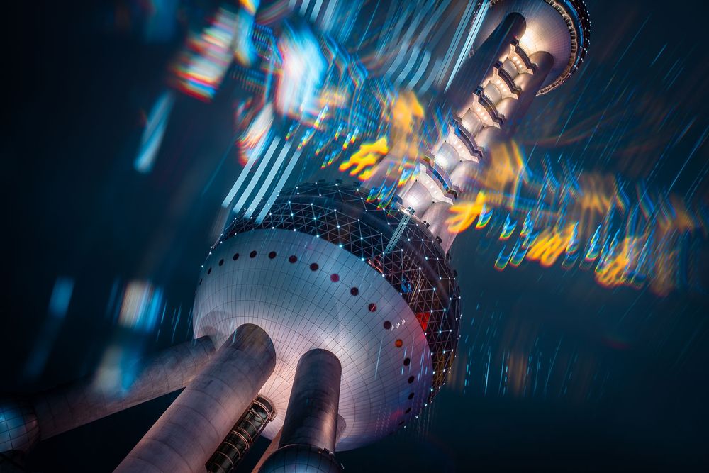 Low-angle long exposure of the illuminated Oriental Pearl Tower with spherical pods and streaking blue and orange city lights at night.