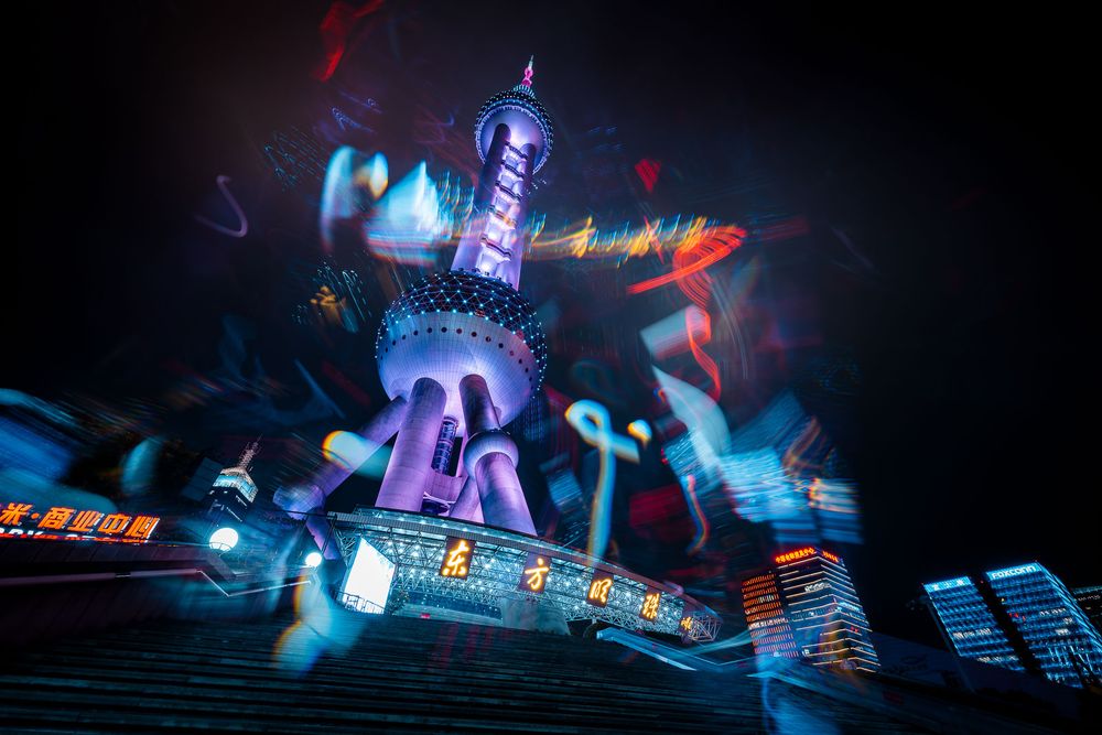 Oriental Pearl Tower in Shanghai glowing in purple and pink neon lights at night with colorful motion blur streaks across the skyline.