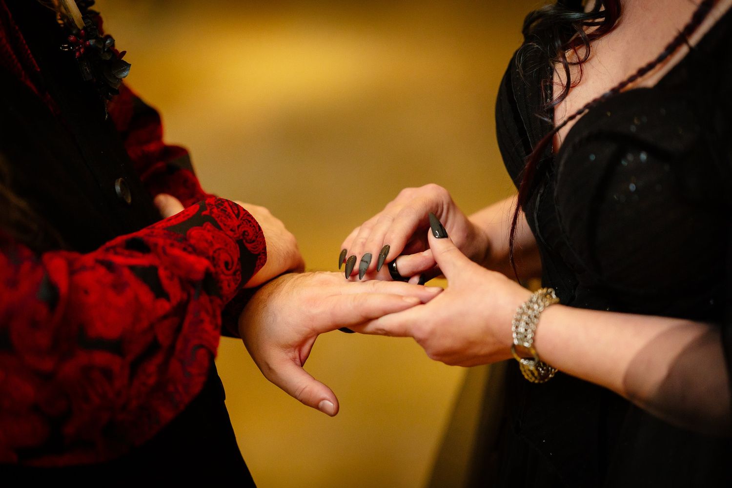 Bride with black nails placing a wedding ring on the groom's finger during a gothic wedding ceremony