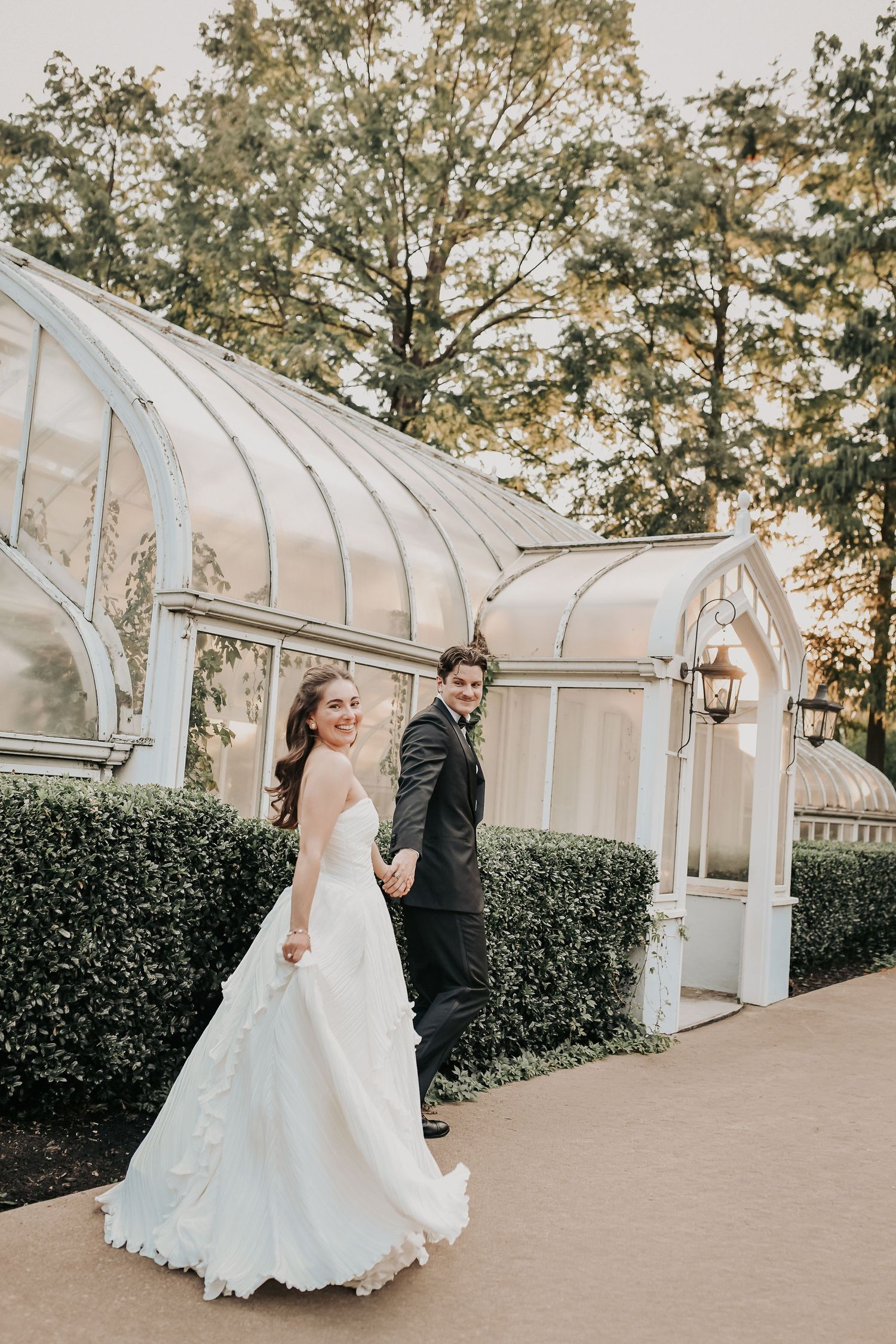 a happy bride and groom pose in front of the glass green house at TWU for their wedding photos