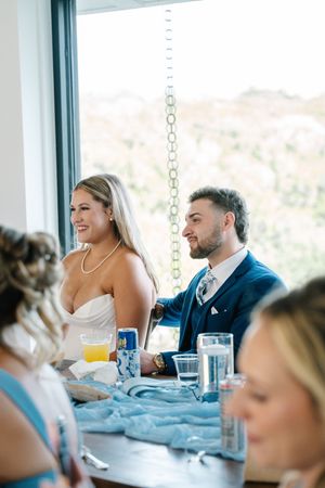 Bride and groom sit together at wedding reception table, smiling and enjoying the celebration.