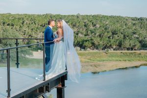 Bride and groom kissing on elevated platform overlooking scenic river and treetop landscape.