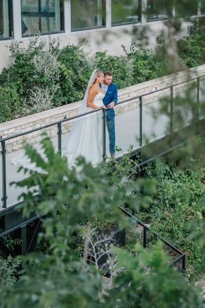 Bride and groom embracing on modern bridge walkway surrounded by lush green foliage.