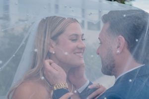 Bride and groom share an intimate moment under a wedding veil, smiling at each other.