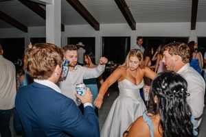Bride in white dress dances joyfully with guests at lively outdoor wedding reception.