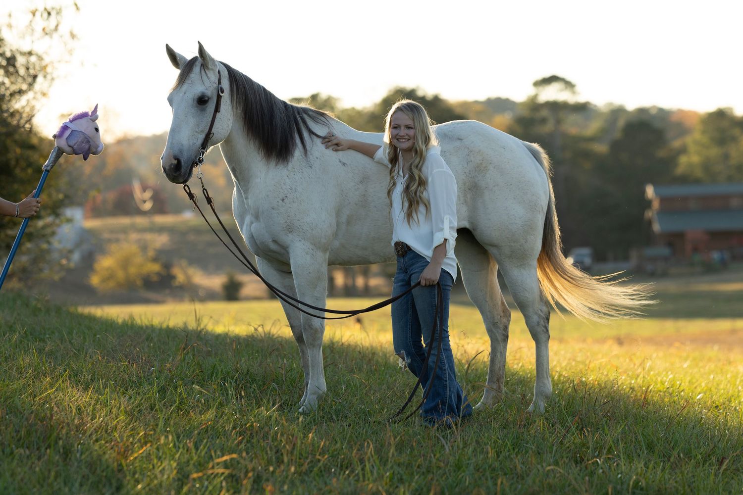 Woman in riding attire stands beside a chestnut horse in a sandy equestrian arena with wooden fencing.