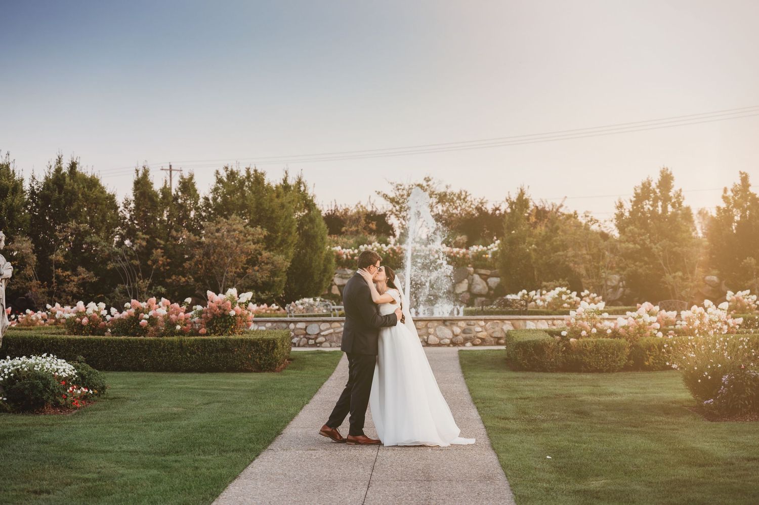 Couple in wedding attire on rocky shoreline surrounded by autumn trees with blue lake views.