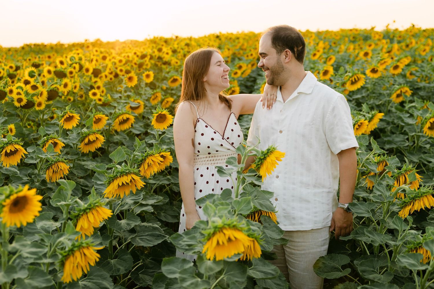 Couple smiling at each other in a vibrant sunflower field in alentejo at golden hour sunset.