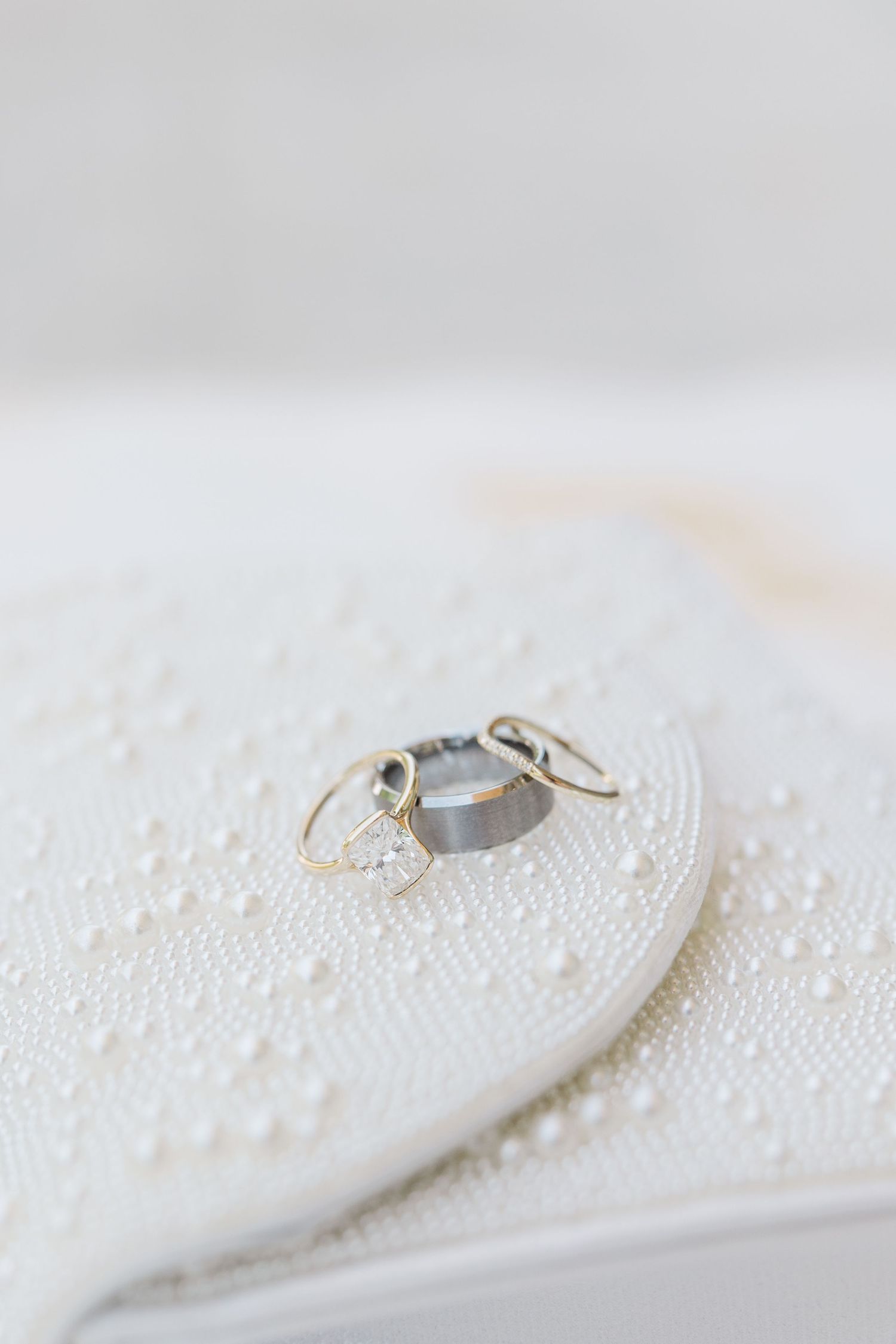 Gold wedding rings and diamond engagement ring displayed on white pearl-embellished surface.