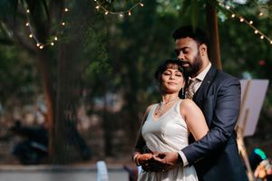 Elegant couple in wedding attire embracing outdoors under string lights at a romantic evening reception.