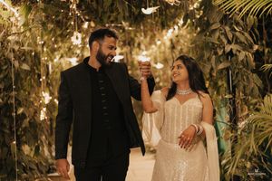 Couple in elegant attire dancing under fairy lights and lush greenery at a romantic evening celebration.