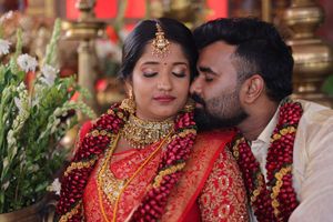 Indian bride in red saree and gold jewelry shares intimate moment with groom during traditional wedding ceremony.