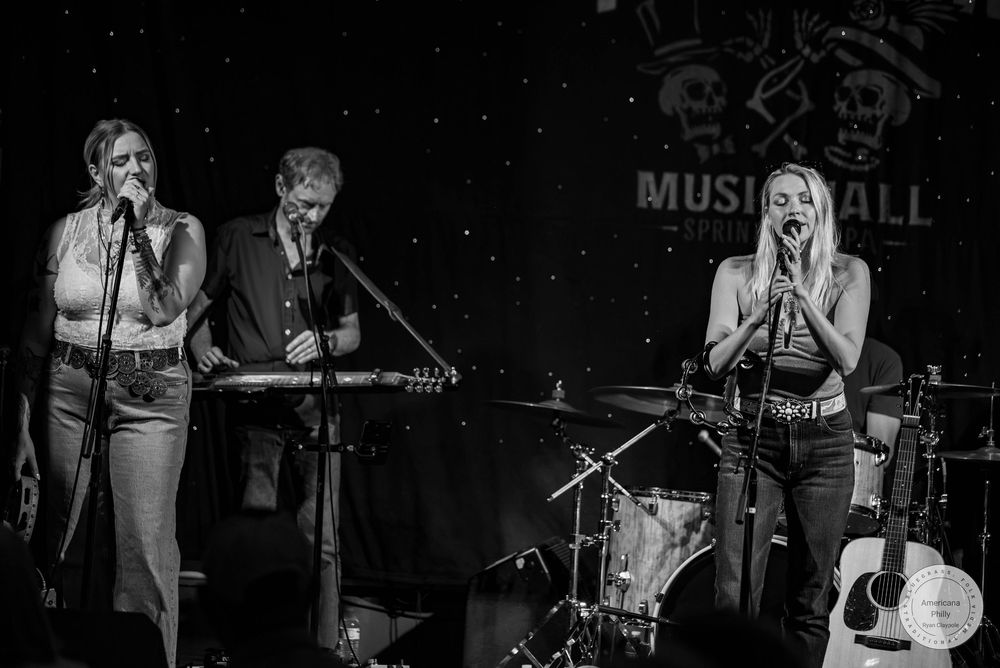 Three musicians perform on stage at a Music Hall venue in a black and white live concert photo.