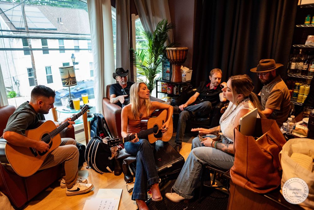 Group of musicians playing acoustic guitars in a cozy indoor setting near a large window.