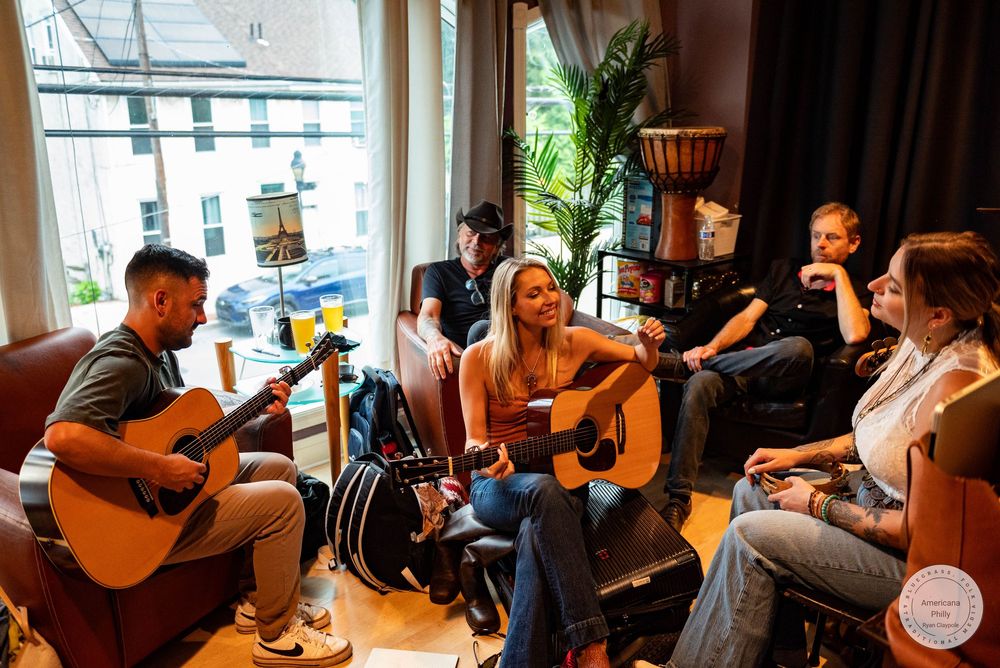 Group of friends playing acoustic guitars and socializing in a cozy music lounge near a bright window.