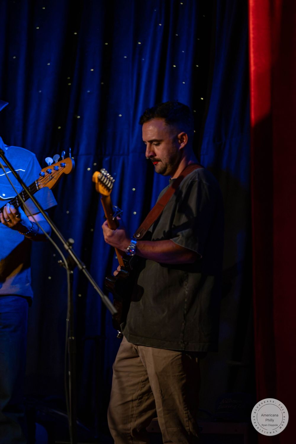 Male guitarist performing on stage under blue and red stage lighting at a live music event.