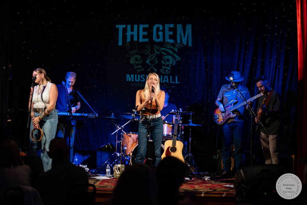 Live band performs on stage at The Gem Music Hall, featuring a female vocalist and guitarist under warm stage lights.