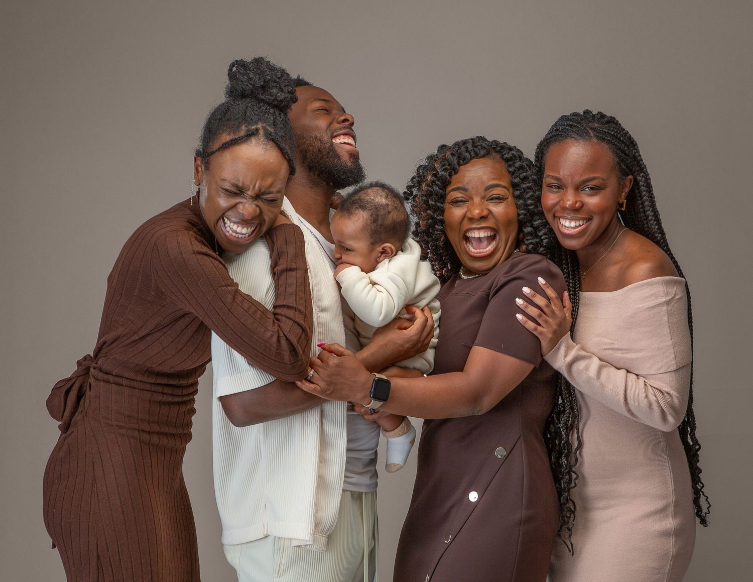 Joyful Black family of five posing together, laughing and embracing, with a baby, in a professional studio portrait.