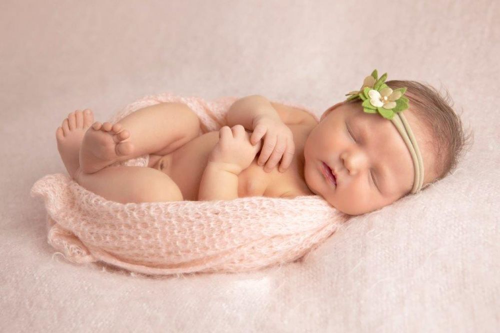 Peaceful newborn baby girl sleeping wrapped in a pink knit blanket with a delicate green flower headband.