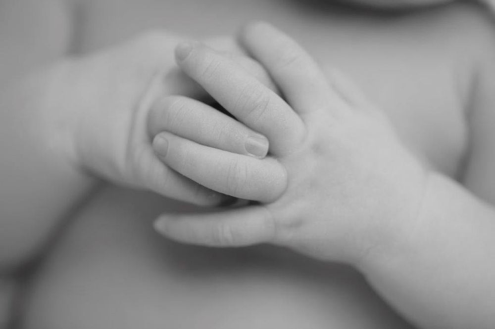 Black and white close-up photo of a newborn baby's tiny hand gently clasped around an adult's finger.