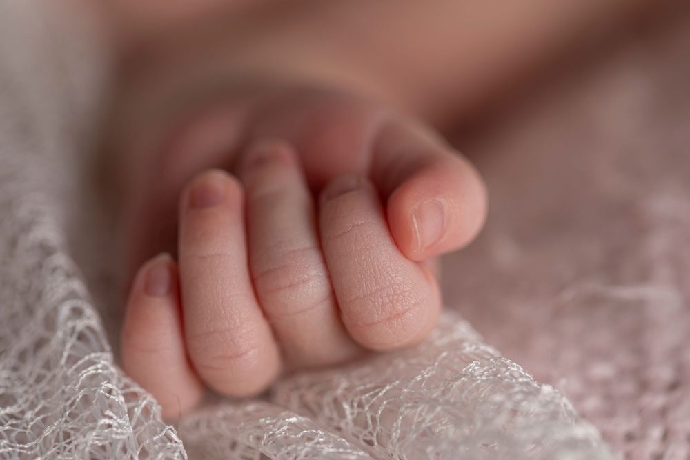 Close-up of a newborn baby's tiny clenched fist resting on a soft pink knit blanket.